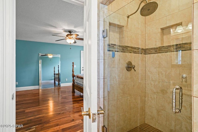 full bathroom featuring a stall shower, ceiling fan, a textured ceiling, wood finished floors, and baseboards