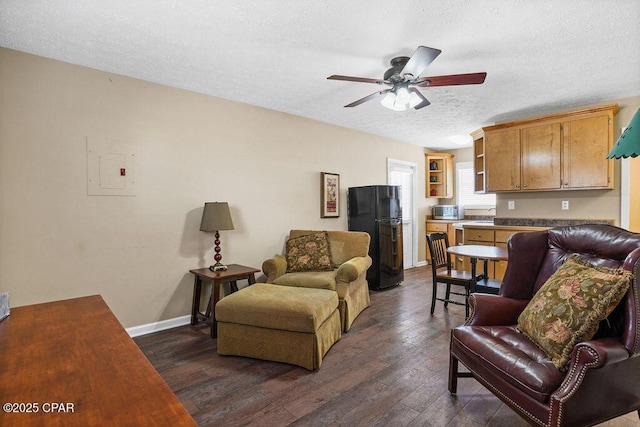 living area with a textured ceiling, dark wood-style flooring, a ceiling fan, and baseboards