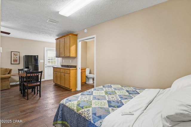 bedroom with dark wood-style floors, freestanding refrigerator, visible vents, and a textured ceiling