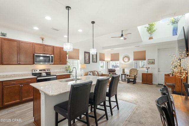 kitchen featuring stainless steel appliances, a ceiling fan, open floor plan, a sink, and a kitchen bar