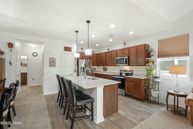 kitchen with light wood finished floors, a kitchen bar, appliances with stainless steel finishes, and decorative light fixtures