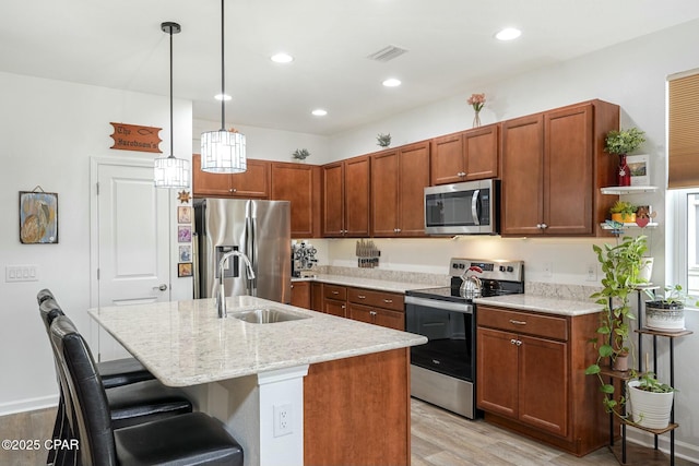 kitchen with appliances with stainless steel finishes, light stone countertops, light wood-style floors, a kitchen bar, and a sink