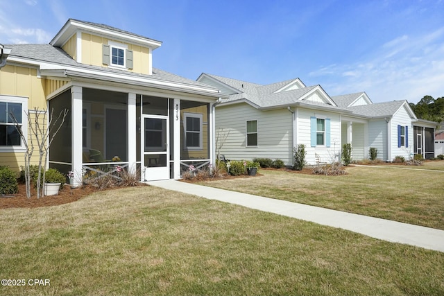 view of front of property with board and batten siding, a front yard, a sunroom, and roof with shingles