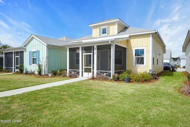 back of house with a sunroom, a shingled roof, board and batten siding, and a yard