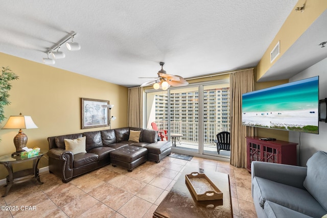 living room featuring light tile patterned floors, a ceiling fan, baseboards, track lighting, and a textured ceiling