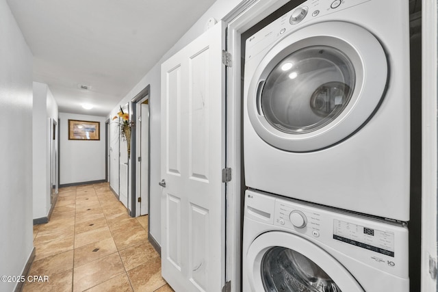 washroom featuring stacked washer / drying machine, baseboards, light tile patterned flooring, and laundry area