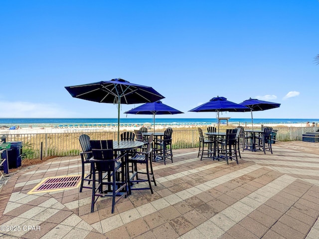 view of patio with a water view, fence, outdoor dining space, and a view of the beach