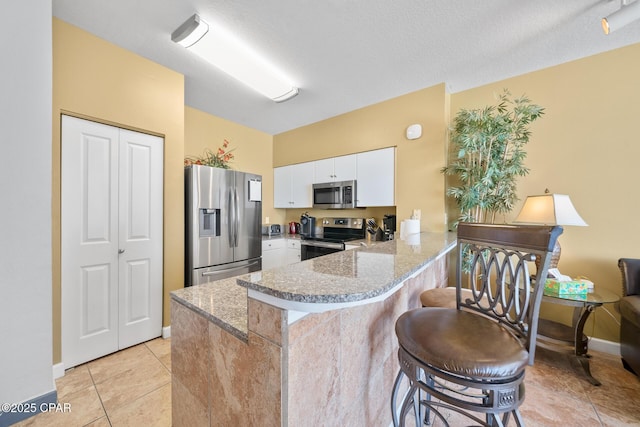 kitchen with a peninsula, white cabinets, light stone countertops, and appliances with stainless steel finishes