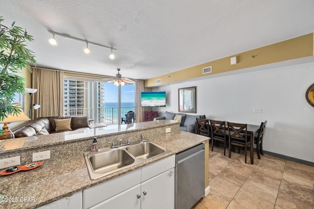 kitchen with a sink, a textured ceiling, open floor plan, white cabinets, and dishwasher