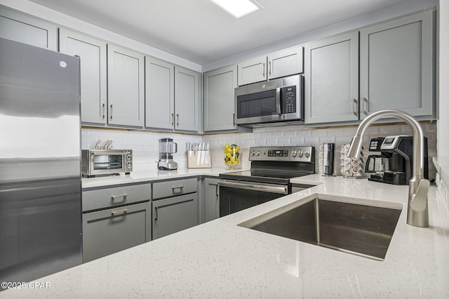 kitchen featuring a toaster, stainless steel appliances, gray cabinets, backsplash, and light stone countertops