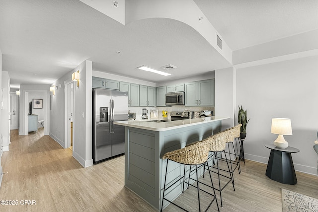 kitchen featuring a breakfast bar, visible vents, light wood-style flooring, appliances with stainless steel finishes, and a peninsula