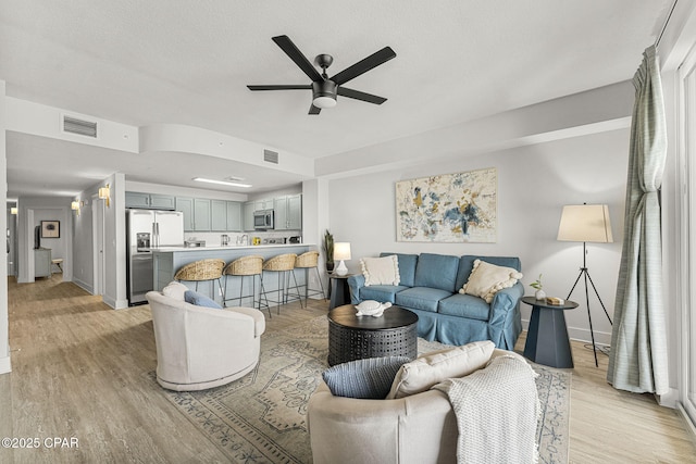 living room with light wood-type flooring, visible vents, and a ceiling fan