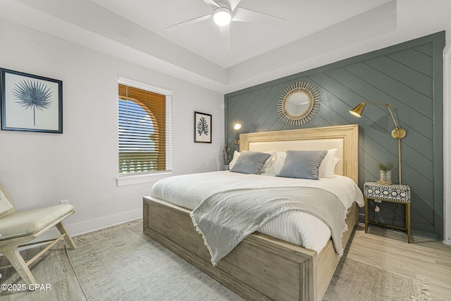 bedroom with an accent wall, wood walls, wood finished floors, a ceiling fan, and baseboards