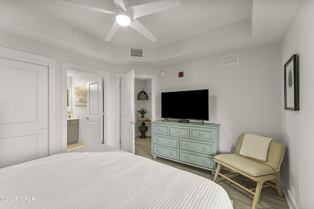 bedroom with a raised ceiling, visible vents, and wood finished floors