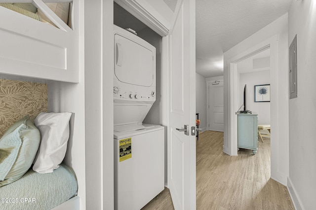 clothes washing area with stacked washer and dryer, light wood-style flooring, baseboards, and a textured ceiling