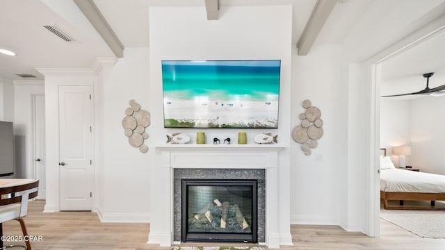 living area featuring light wood-type flooring, visible vents, beam ceiling, and a glass covered fireplace