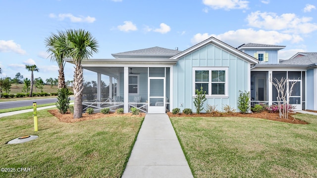 view of front of home with board and batten siding, a front yard, a sunroom, and roof with shingles