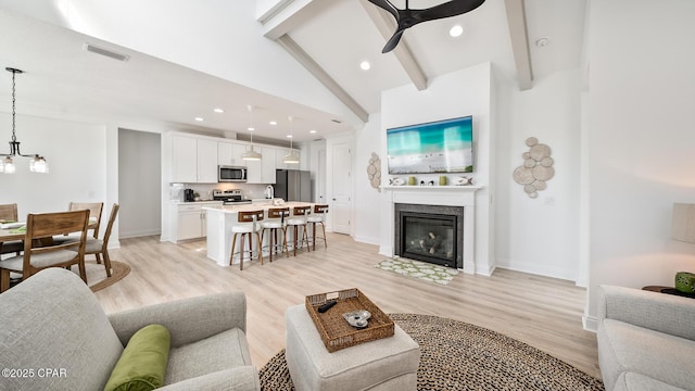 living area featuring light wood-style flooring, beamed ceiling, visible vents, and a ceiling fan