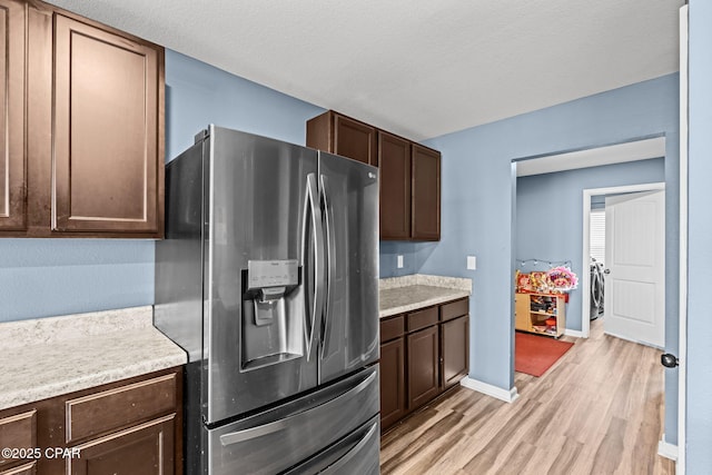 kitchen with light wood-style flooring, dark brown cabinetry, baseboards, light countertops, and stainless steel fridge