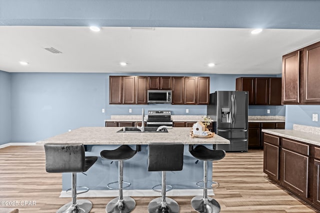 kitchen with appliances with stainless steel finishes, a sink, light wood finished floors, and a breakfast bar area