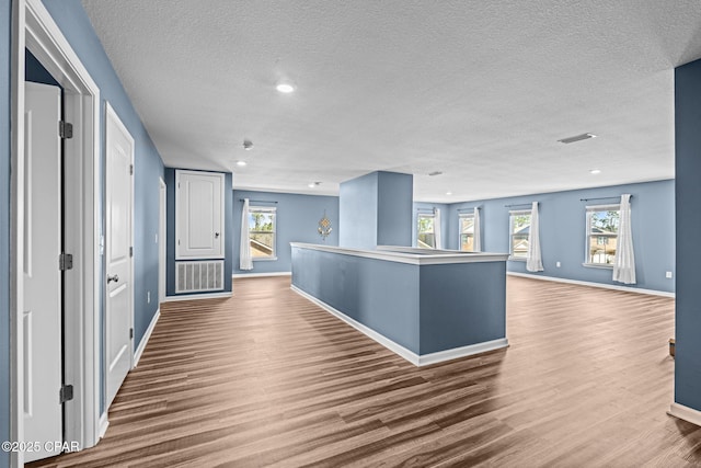 hall with baseboards, a textured ceiling, visible vents, and wood finished floors