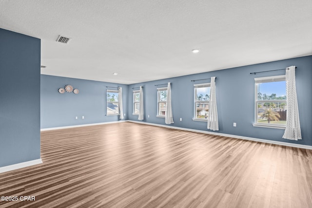 unfurnished living room with a textured ceiling, wood finished floors, visible vents, and baseboards