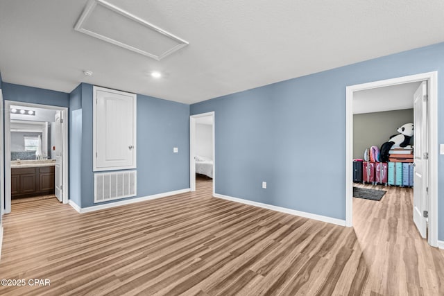 unfurnished bedroom with visible vents, light wood-style flooring, ensuite bathroom, attic access, and baseboards