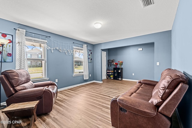 living area with visible vents, a textured ceiling, baseboards, and wood finished floors