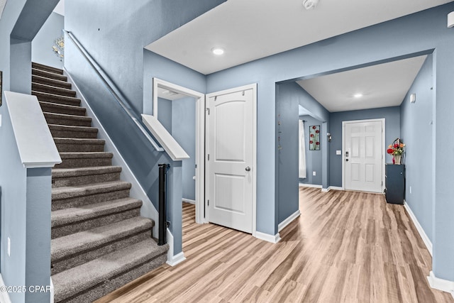 foyer with light wood-type flooring, baseboards, and stairs