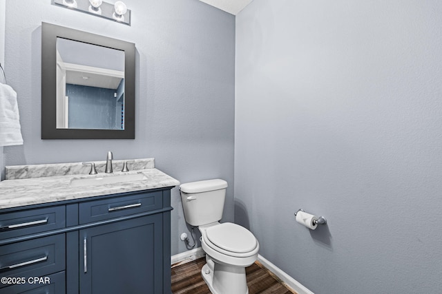 half bath featuring vanity, wood finished floors, toilet, and baseboards