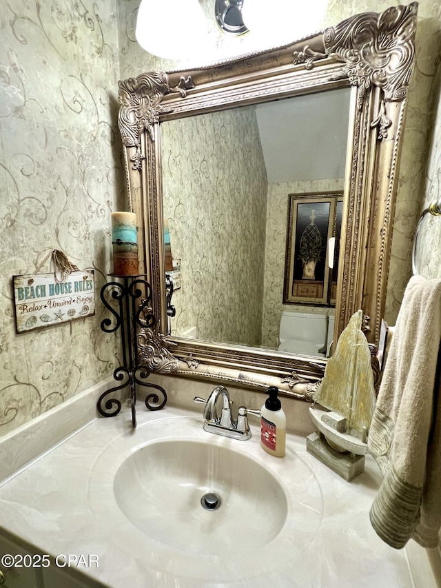 bathroom with vanity, toilet, and wallpapered walls