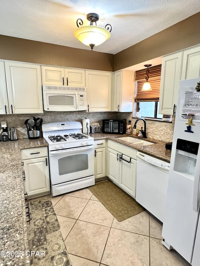 kitchen featuring light tile patterned floors, backsplash, white cabinetry, a sink, and white appliances