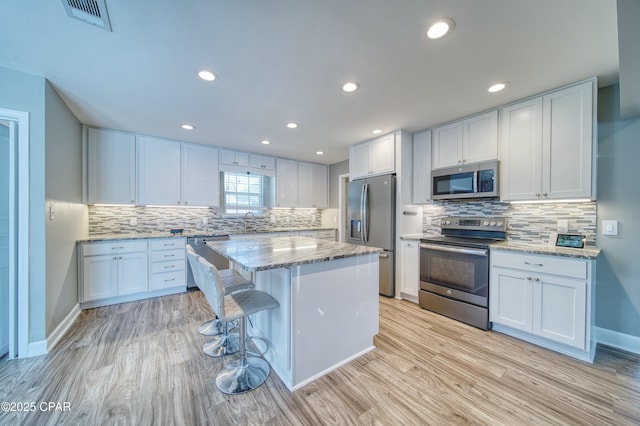 kitchen with appliances with stainless steel finishes, a kitchen island, light stone counters, and light wood finished floors