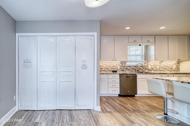 kitchen featuring decorative backsplash, light stone counters, light wood-type flooring, white cabinetry, and stainless steel dishwasher