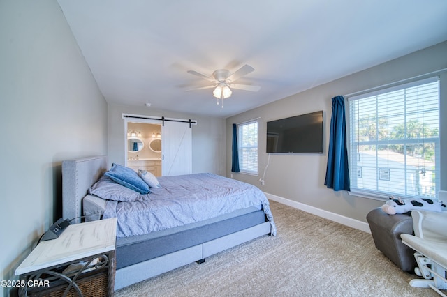 carpeted bedroom featuring a barn door, connected bathroom, baseboards, and a ceiling fan