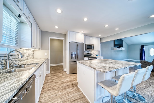 kitchen featuring a center island, stainless steel appliances, white cabinets, a sink, and light stone countertops