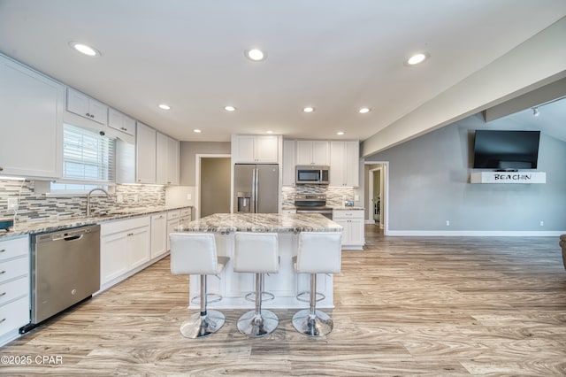 kitchen featuring a center island, stainless steel appliances, white cabinets, a sink, and light stone countertops