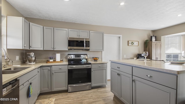 kitchen with light wood-style flooring, a kitchen island, appliances with stainless steel finishes, gray cabinets, and a sink