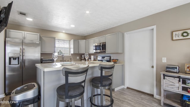 kitchen featuring a textured ceiling, a breakfast bar area, stainless steel appliances, visible vents, and light countertops