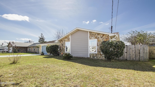 view of side of property featuring a lawn, fence, a garage, stone siding, and driveway