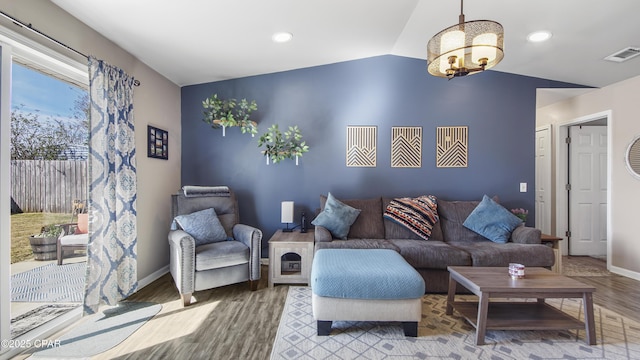 living room featuring lofted ceiling, a notable chandelier, wood finished floors, visible vents, and baseboards