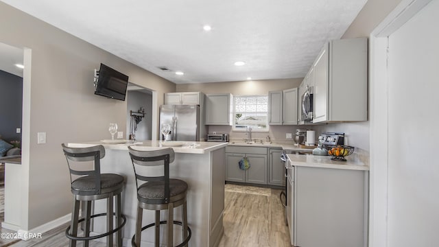 kitchen featuring appliances with stainless steel finishes, a kitchen breakfast bar, light countertops, gray cabinets, and a sink