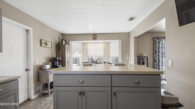 kitchen with light wood-style flooring, a kitchen island, visible vents, and gray cabinetry