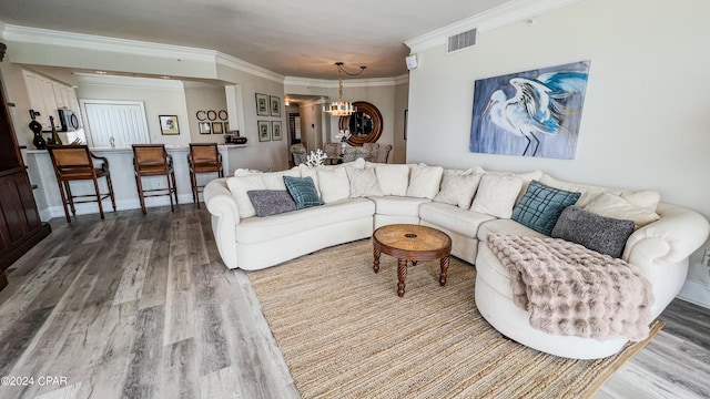 living area with baseboards, visible vents, ornamental molding, wood finished floors, and a chandelier