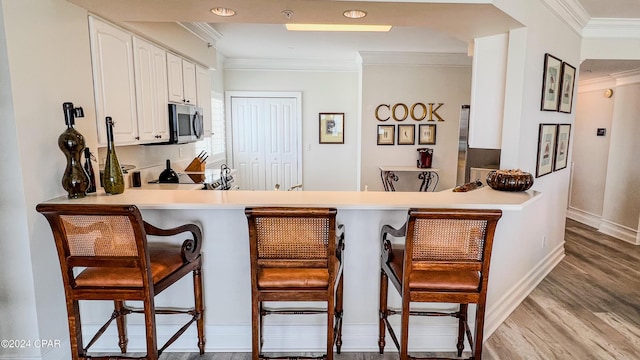 kitchen with crown molding, stainless steel microwave, white cabinetry, wood finished floors, and a peninsula