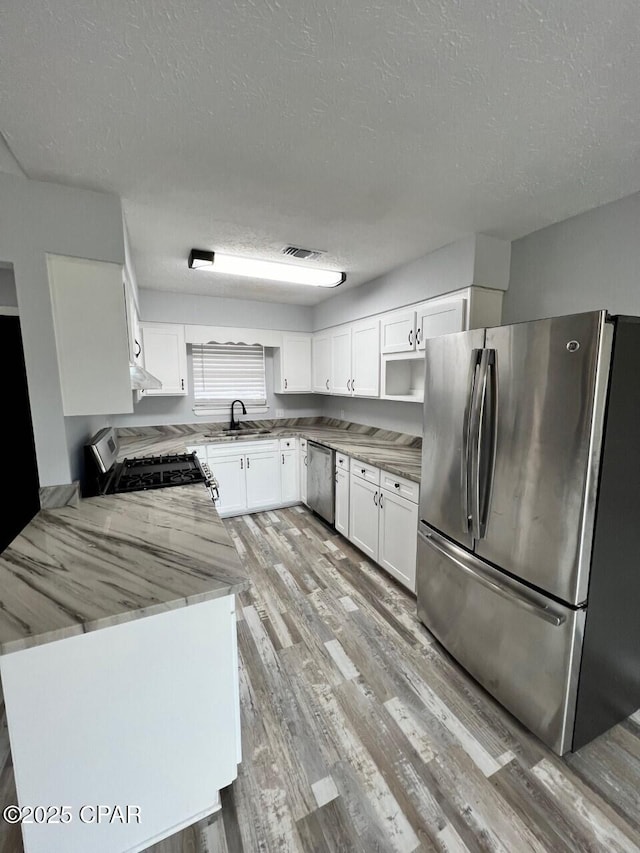 kitchen with light stone counters, light wood finished floors, a sink, white cabinets, and appliances with stainless steel finishes