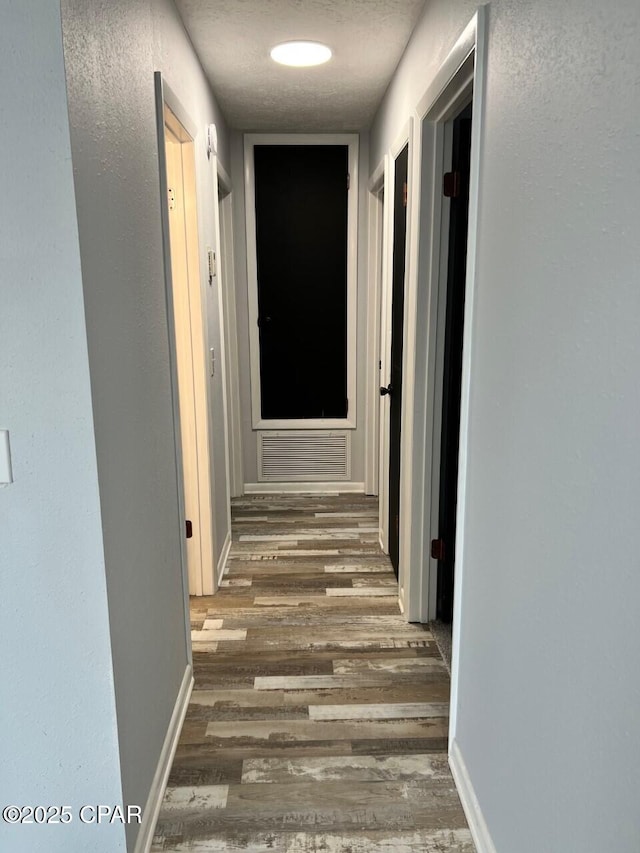 corridor with wood finished floors, visible vents, and baseboards