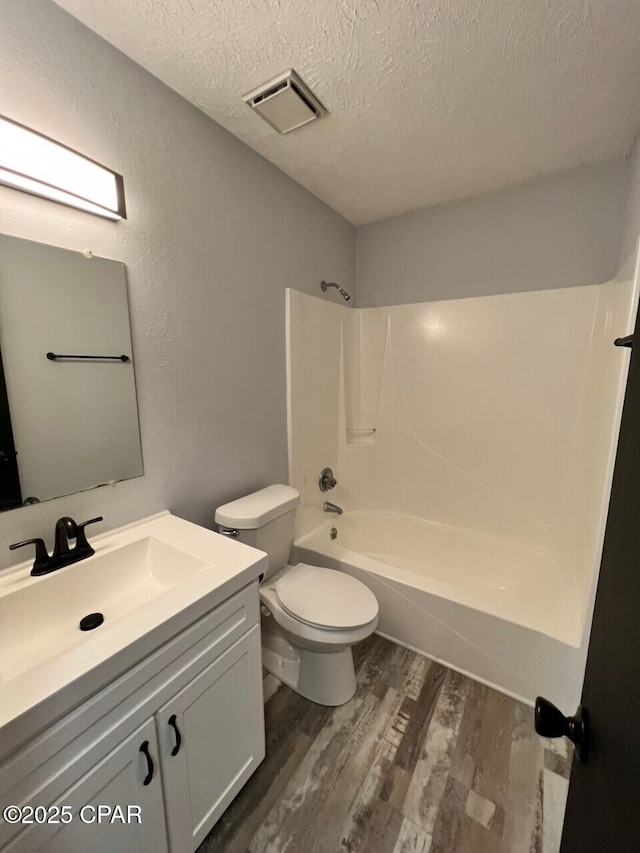 bathroom with vanity, wood finished floors, visible vents, a textured ceiling, and toilet