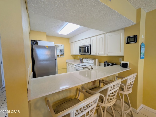 kitchen featuring light tile patterned floors, a textured ceiling, a breakfast bar, white cabinetry, and appliances with stainless steel finishes