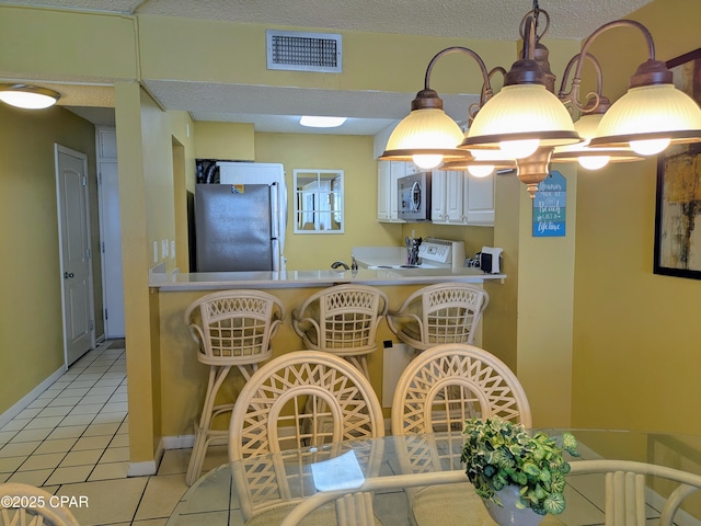 kitchen featuring visible vents, hanging light fixtures, stainless steel appliances, a textured ceiling, and light tile patterned flooring